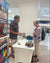 Two people interacting at a table with board game boxes in a store setting.